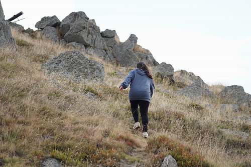 person woman in gray jacket climbing a mountainside outdoors