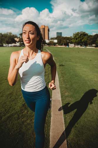 person woman in white tank top and blue leggings jogging in grass field female