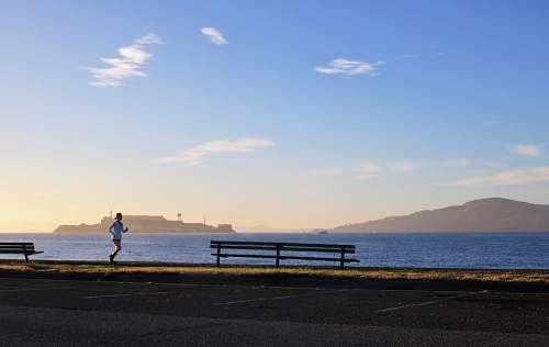 person woman jogging near ocean bench