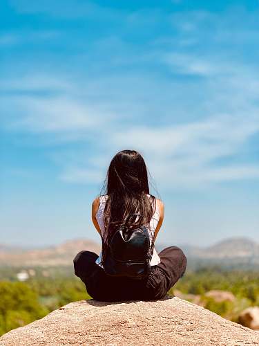 person woman sitting on rock facing the field during day outdoors