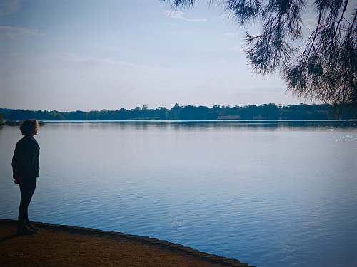 person woman standing alone facing body of water people