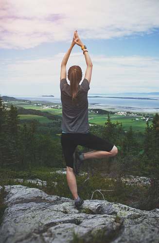 person woman standing on one leg on rock facing the field exercise