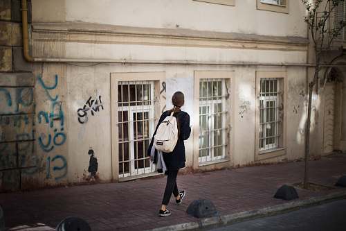 person woman walking on sidewalk nearby beige structure people