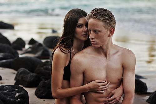 person woman wearing bikini top standing at the back of topless man beside rocks apparel
