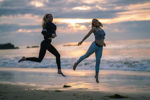 person woman wearing blackjacked and black leggings jumping on seashore sports