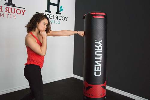 person woman wearing red tank top punching black Century heavy bag cylinder