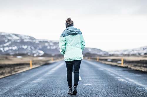 people woman wearing teal jacket and black pants walking on concrete road person