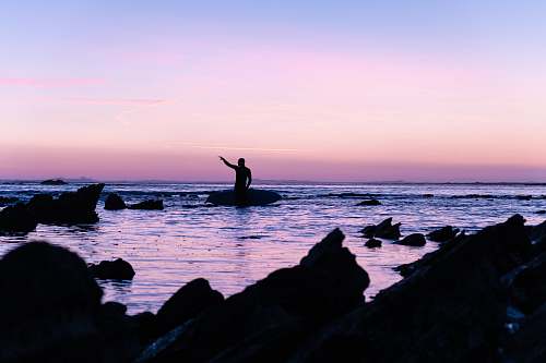 water silhouette of person standing on rock beside beach outdoors