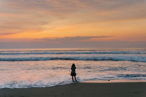 coast silhouette of woman standing beside seashore sea