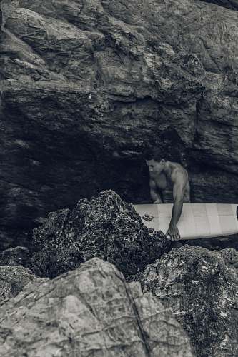 nature man holding surfboard beside rock rock