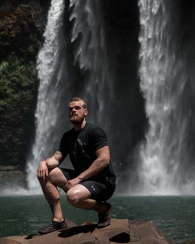 nature man sitting on rock near waterfalls river