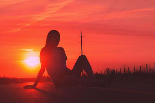 nature silhouette of woman sitting in road during golden hour sky