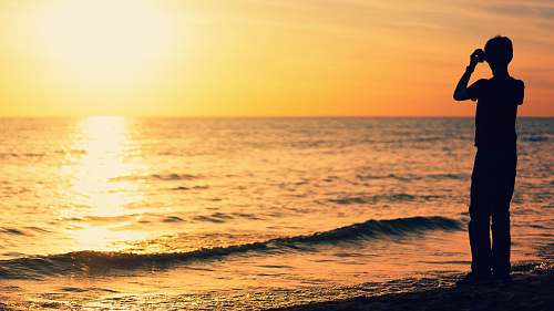 nature silhouette photography of boy on seashore during golden hour ocean