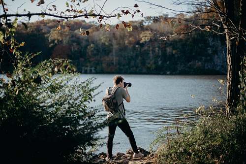person man with backpack taking picture beside lake human