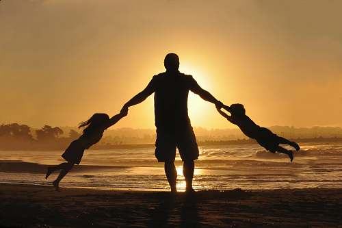 family silhouette of man holding two childrens on shore during daytime silhouette