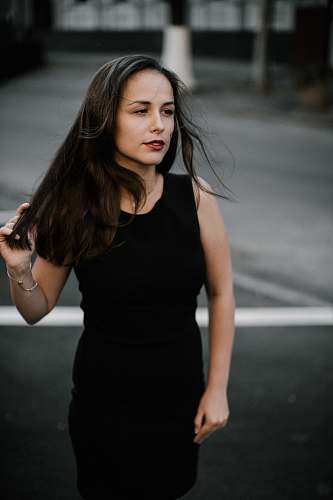 human focus photo of woman in black sleeveless dress walks on road people