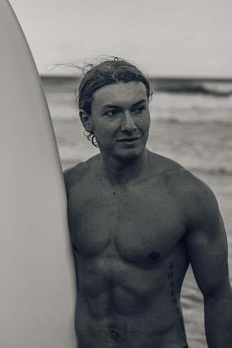 human grayscale photo of man holding surfboard skin