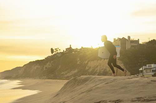 human man carrying white bodyboard on gray sand beach people