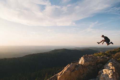 hiking man jumping on brown rock mountain during daytime mountain