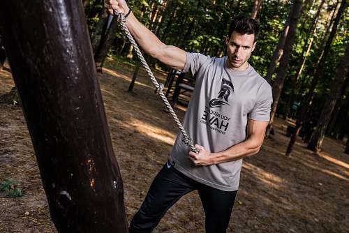 human man pulling gray rope beside tree trunk in forest people
