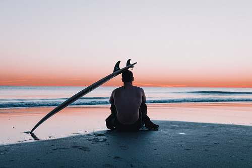 human man sitting on the sand in front of sea nature