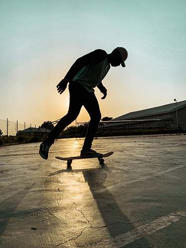 human man skateboarding on cemented vacant lot during sunset sport