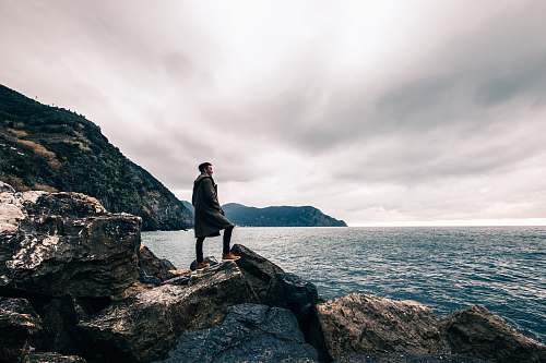 human man standing on boulder near body of water people
