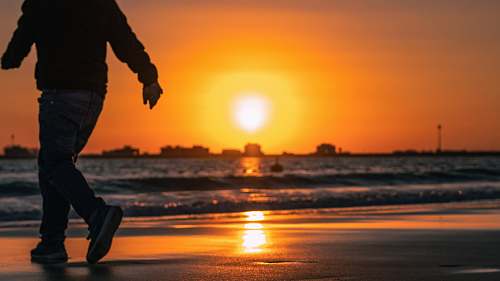 human man walking on seashore during sunset apparel