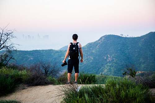 human man wearing black backpack standing near mountain at daytime people