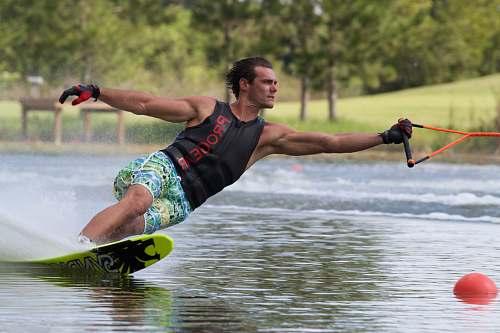 human man wearing gloves and black tank top while water skiing people