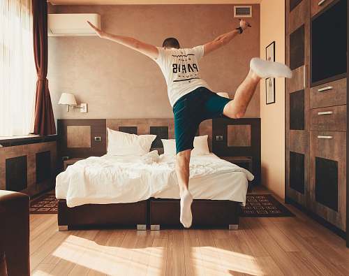 human man wearing white shirt about to jump on bed flooring