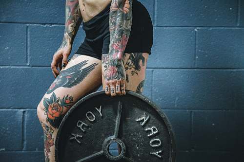 people person carrying black weight plate with right hand tattoo