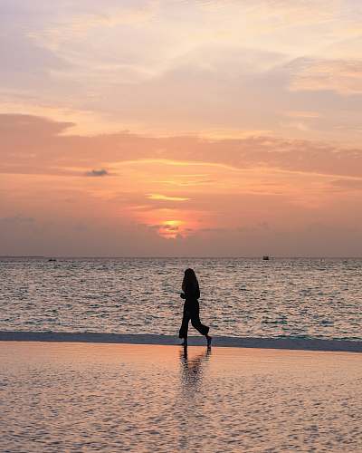 human person jogging on seashore under orange sky nature