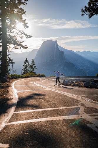 human person skating on road viewing mountain under blue and white skies asphalt