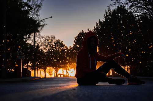 human silhouette of woman sitting on road during golden hour apparel