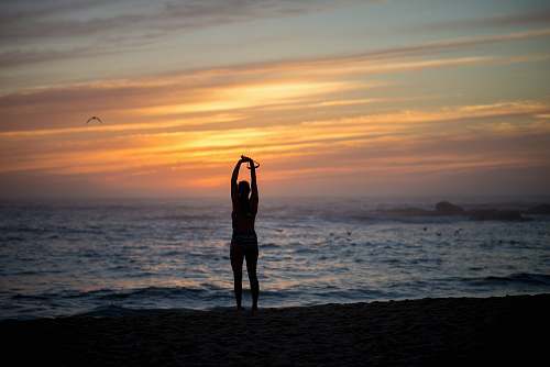 sport silhouette of woman standing beside seashore during sunset working out