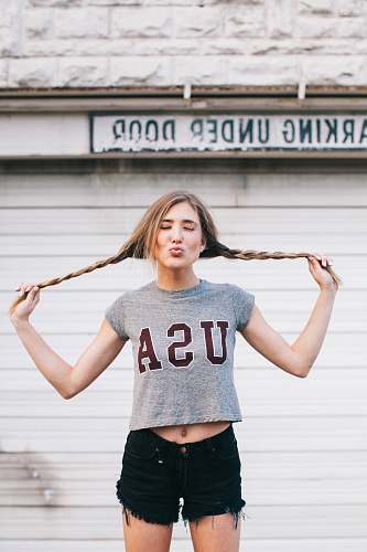 people standing woman holding her pig tail tied hair pouting her lips in front of building woman