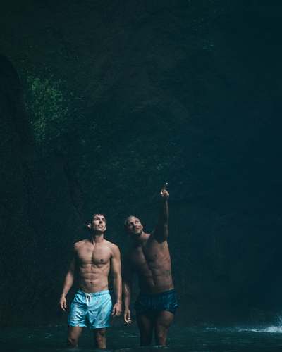 human two men standing on body of water inside cave people