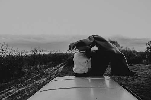 human two person sitting on top of vehicle grayscale photography black-and-white