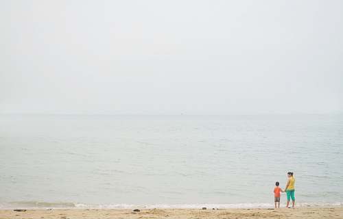 human woman and boy standing on seashore during daytime grey