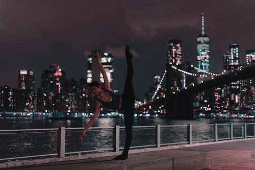 human woman in black sports bra and tights doing ballet position on sidewalk during nighttime dance