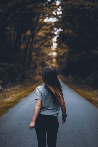 human woman walking on empty road between trees apparel