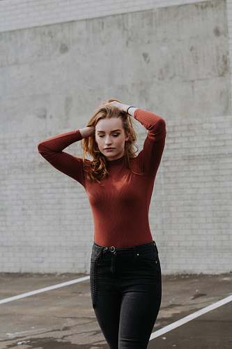 human woman walking while holding her hair near brick wall during daytime people
