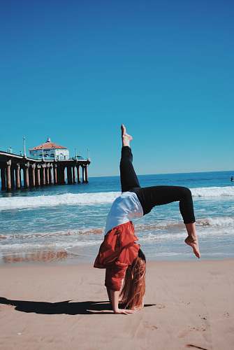 beach woman wearing red jacket and black leggings doing hand stand in seashore sea