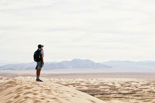 person man standing and carrying backpack in desert land desert