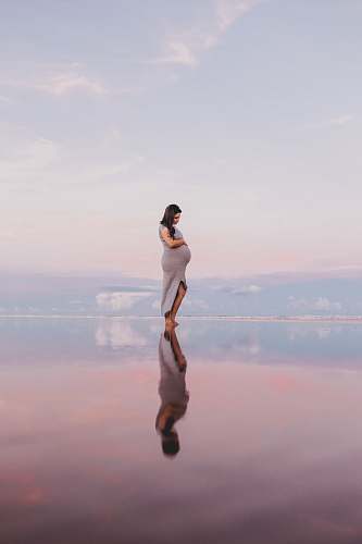person pregnant woman standing on calm body of water human